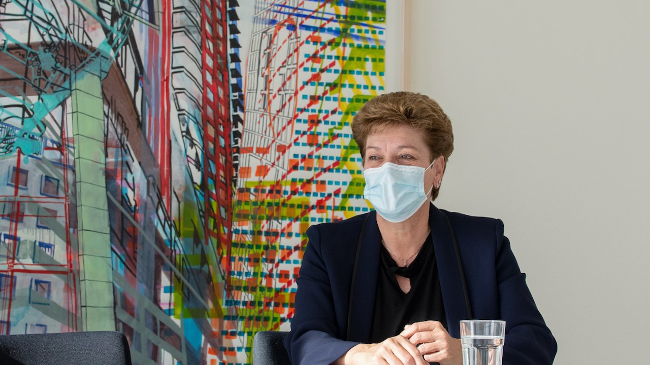 EDK-Präsidentin sitzt mit Hygienemaske vor einem bunten Bild