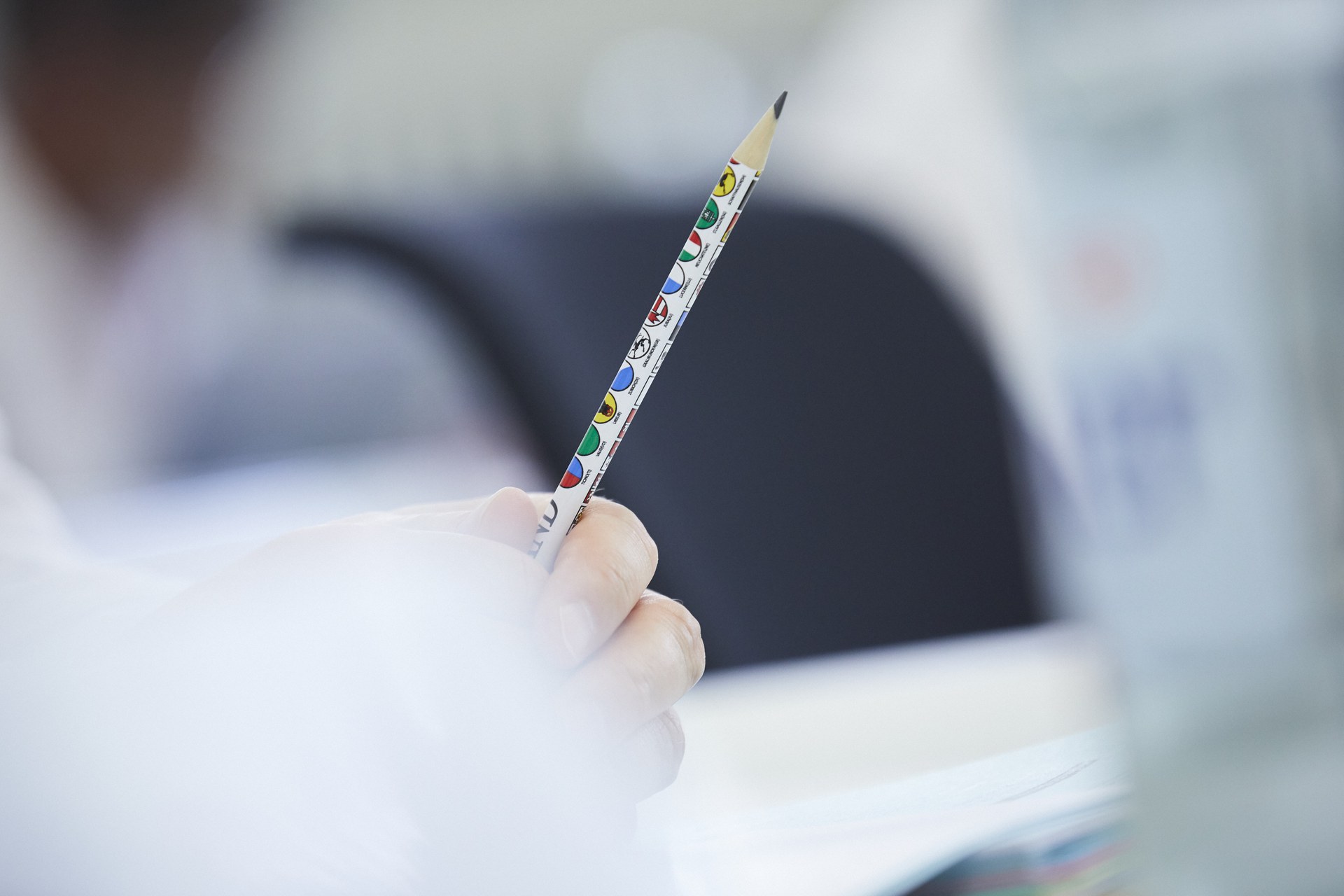 Hand holding a pencil with various cantonal coats of arms on it