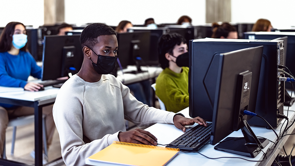 Schülerinnen und Schüler tragen eine Maske und schreiben am Computer einen Test